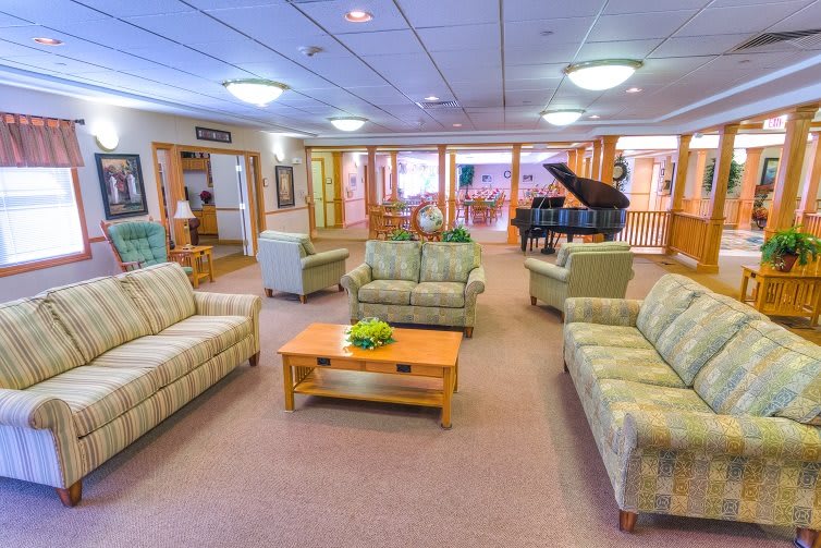 A spacious and well-lit living room featuring multiple sofas, a coffee table, and a grand piano.