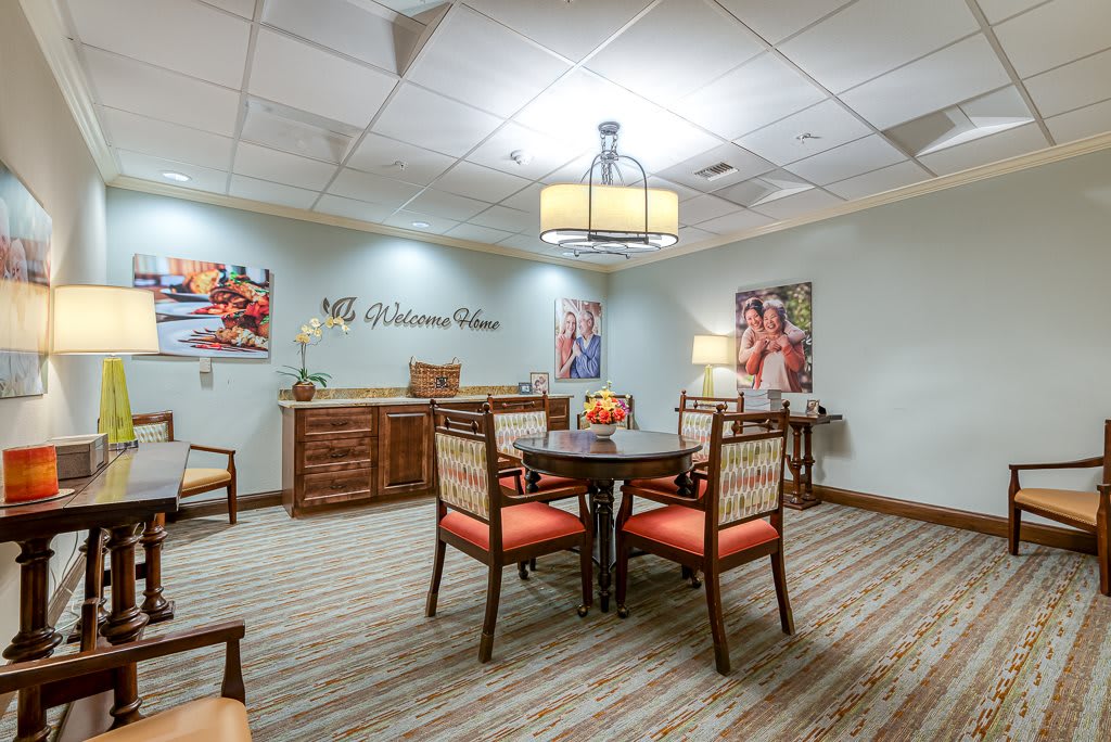 A cozy waiting room with a central table surrounded by chairs, featuring wall decor and warm lighting.