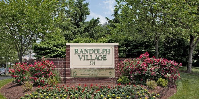 Entrance sign for Randolph Village surrounded by lush greenery and flowers.