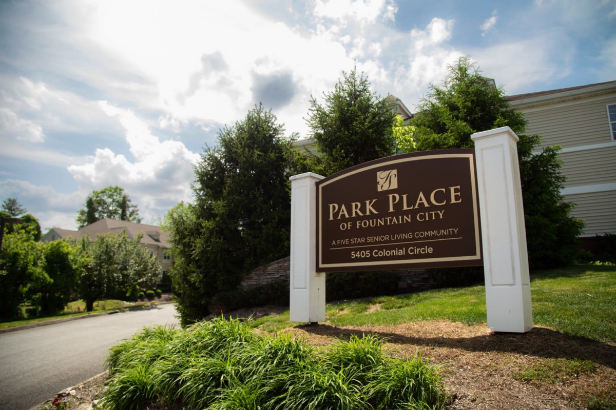 Entrance sign for Park Place apartment complex surrounded by trees and a cloudy sky.