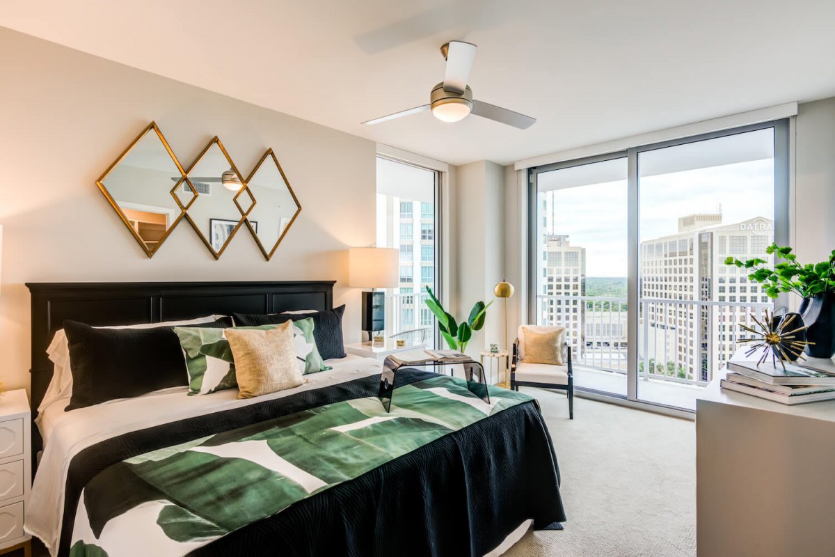 A modern luxury bedroom with large windows overlooking a cityscape, featuring stylish decor and furnishings.