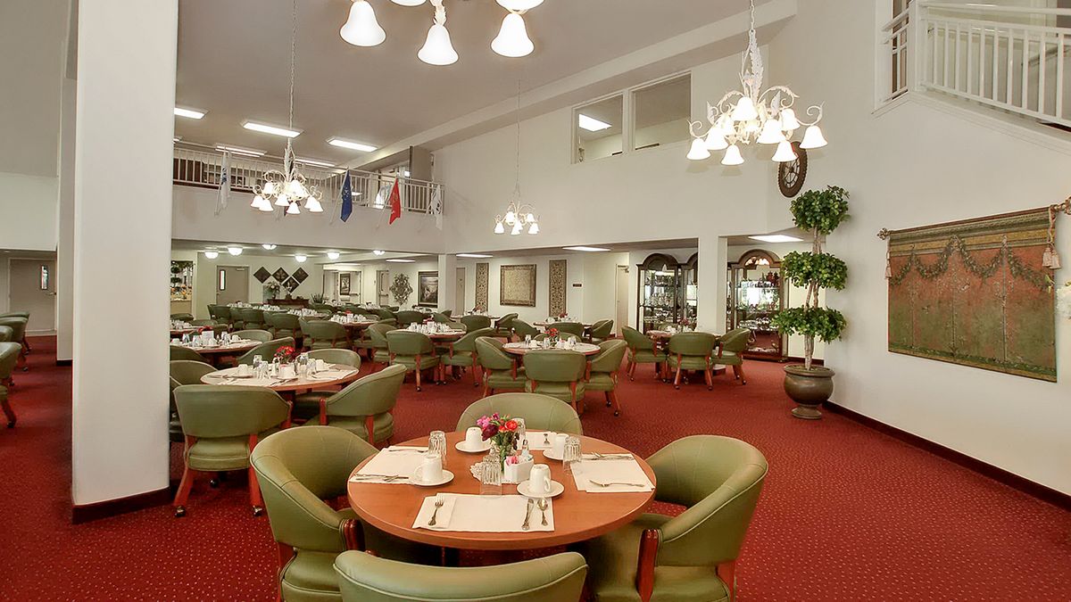 A spacious restaurant dining area with round tables, comfortable chairs, and elegant chandeliers.