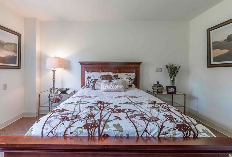A neatly arranged bedroom with a bed featuring floral-patterned bedding, flanked by nightstands and a lamp.
