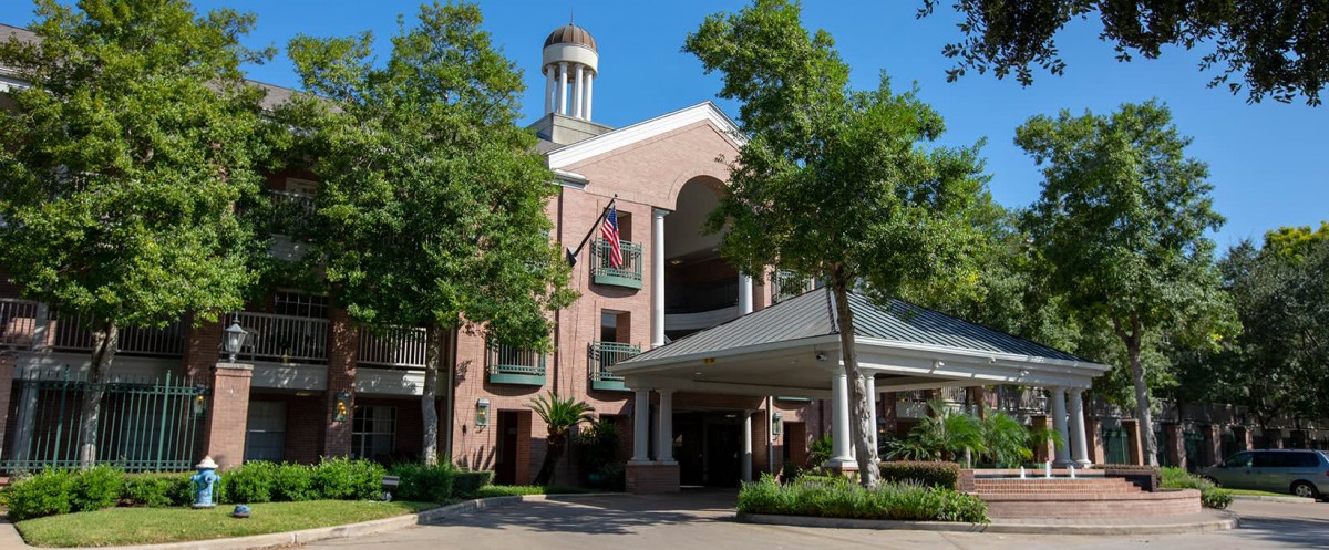 A charming brick hotel entrance with surrounding trees and flags displayed.