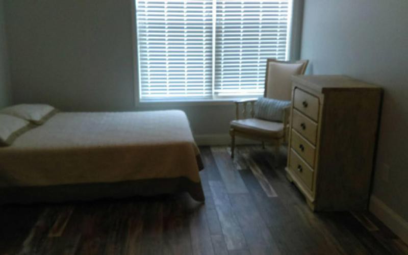 A simple bedroom with a bed, chair, dresser, and window with blinds.