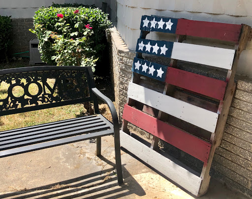 A creatively designed flag made from wooden pallets beside a bench in an outdoor setting.