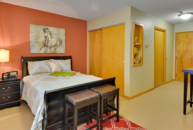 A cozy bedroom featuring a bed with two stools at the foot, a decorative painting on the wall, and built-in closet storage.