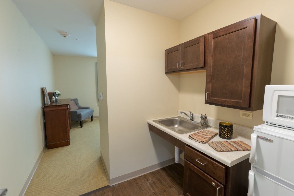 A small kitchenette with a sink, dark wooden cabinets, and a countertop in an apartment setting.