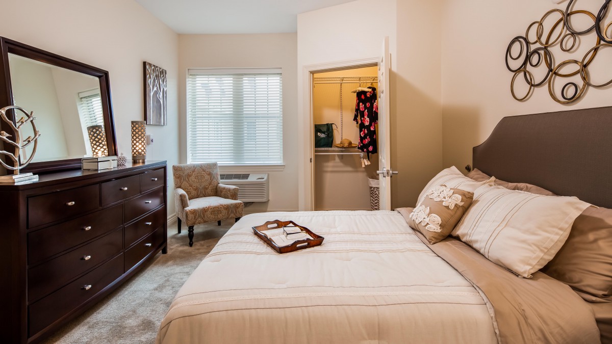 A cozy bedroom with a neatly made bed, a chair by the window, and a dresser.
