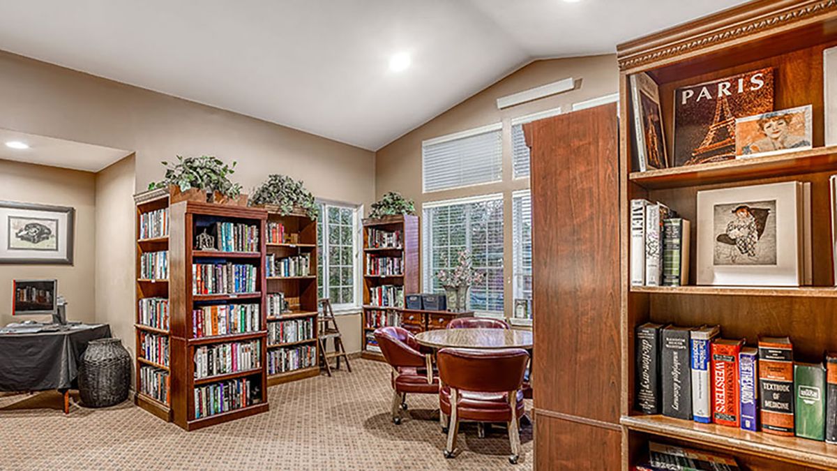 A cozy library corner with bookshelves, a round table, and chairs near large windows.
