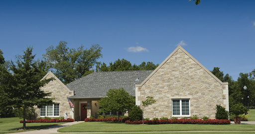 A beautiful single-story house with a stone exterior, surrounded by lush landscaping under a clear blue sky.