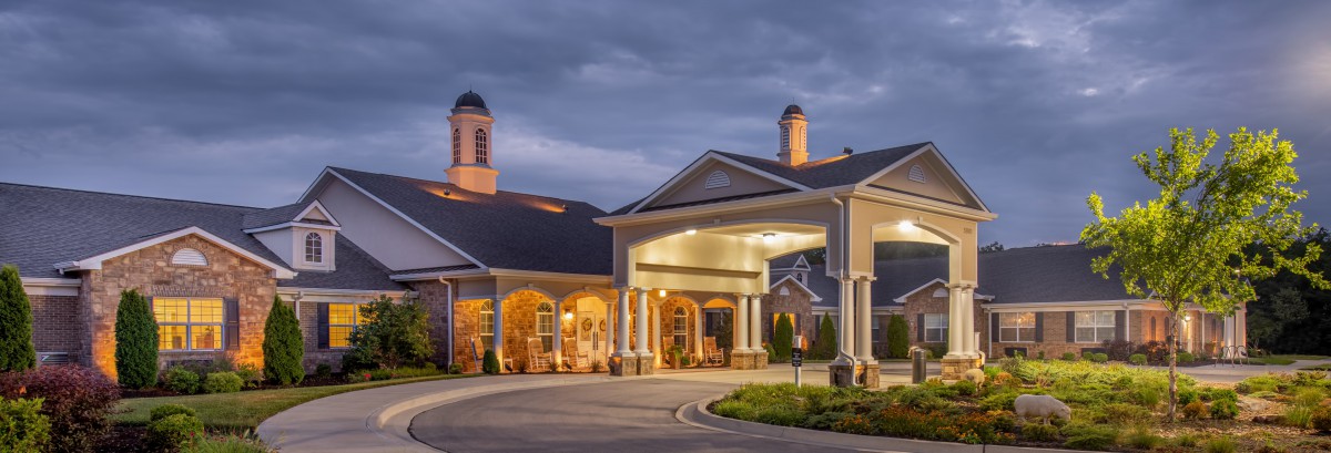 A well-lit building entrance with a driveway during the evening.