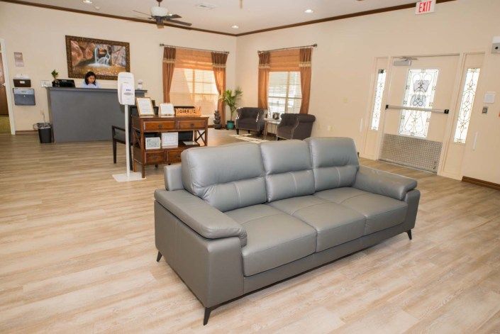 A modern living room or office reception area with a gray sofa and wooden flooring.