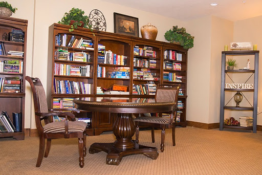 A cozy home office featuring a wooden bookshelf filled with books, a round table, and comfortable chairs.