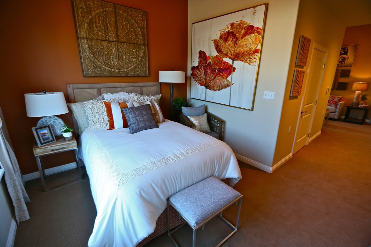 A cozy bedroom featuring a neatly made bed with colorful pillows, warm-toned walls, and decorative artwork.