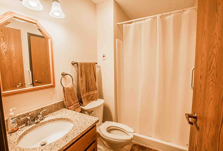 A neatly organized bathroom with a sink, mirror, toilet, and shower area.
