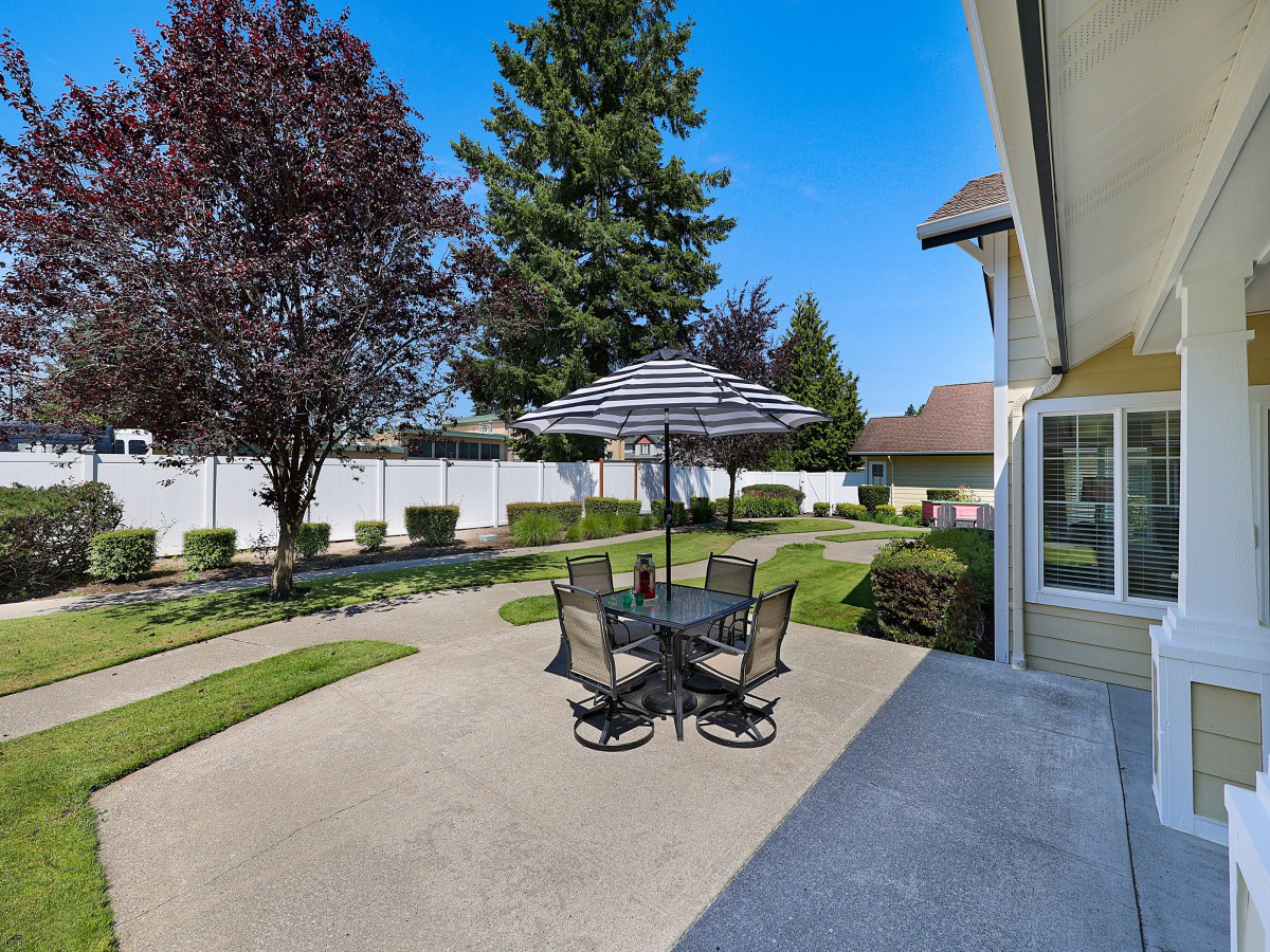 A sunny backyard patio with a table, chairs, and an umbrella.