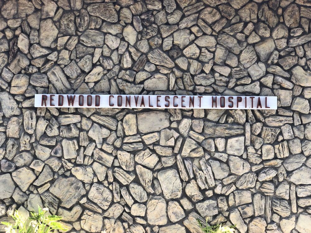 A sign saying 'REDWOOD CONVALESCENT HOSPITAL' on a stone wall background.