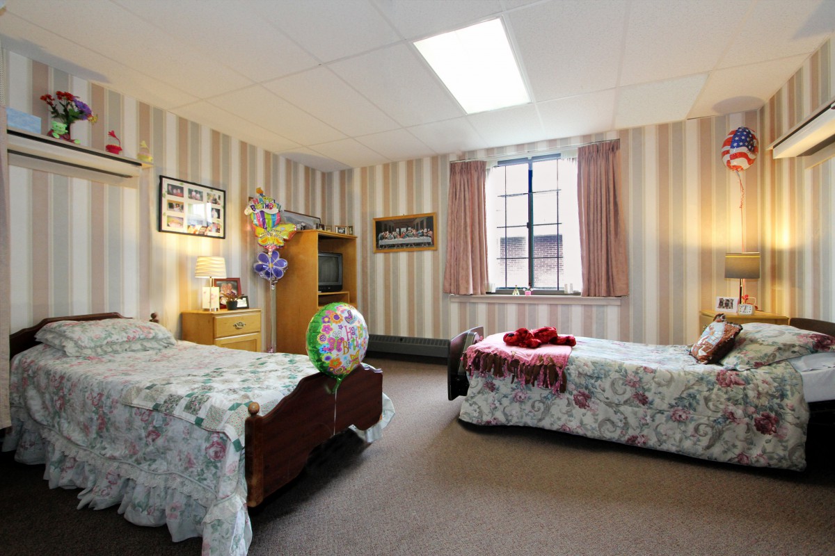 A cozy bedroom with twin beds adorned with floral bedding, featuring striped wallpaper and a large window.