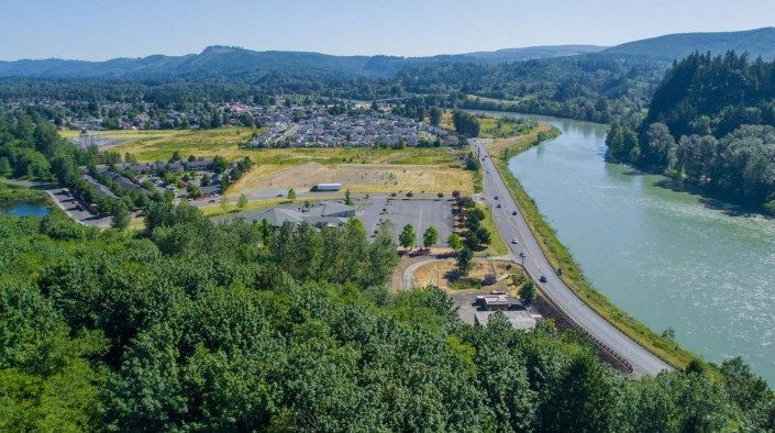 A scenic aerial view of a town nestled between lush greenery and a winding river, with distant rolling hills.