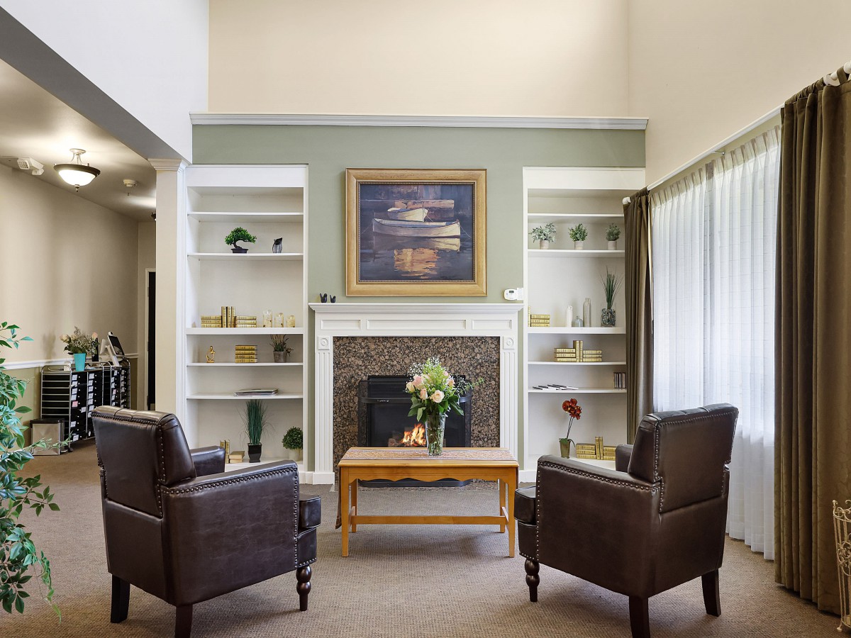 A cozy living room with a fireplace, two armchairs, and built-in bookshelves adorned with decorative items.