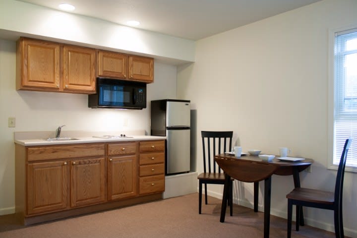 A compact kitchen and dining area featuring wooden cabinets, a microwave, and a small refrigerator.