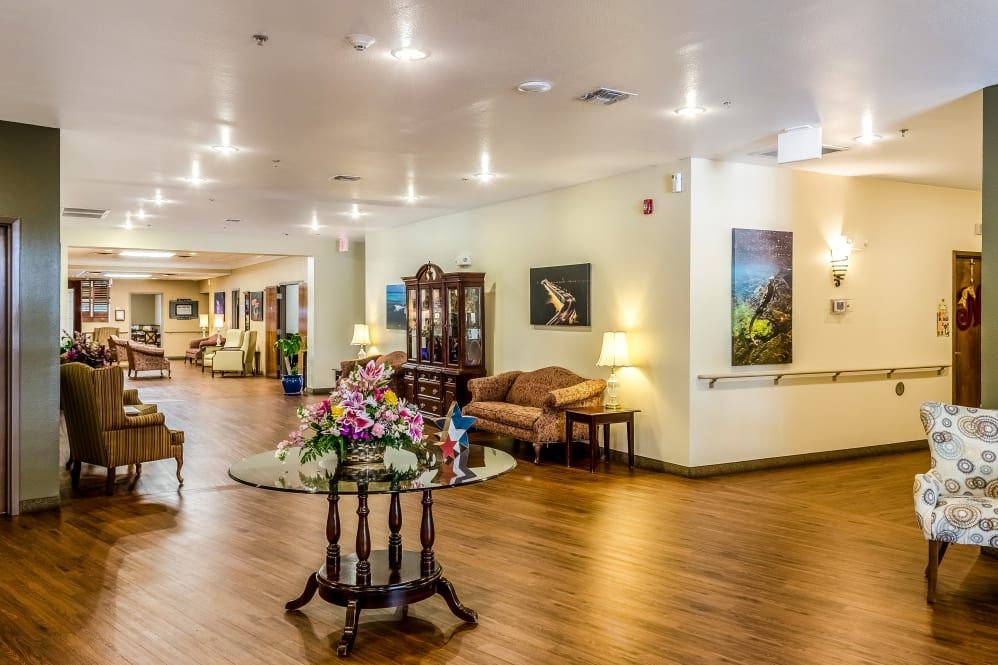 A well-lit lobby area featuring a central table with floral decorations, surrounded by comfortable seating and artwork on the walls.