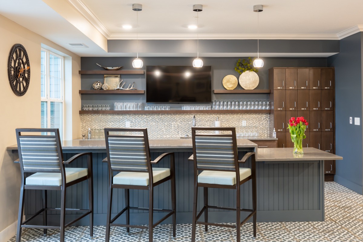A modern home bar area with stylish bar stools, a large countertop, and decorative shelving.