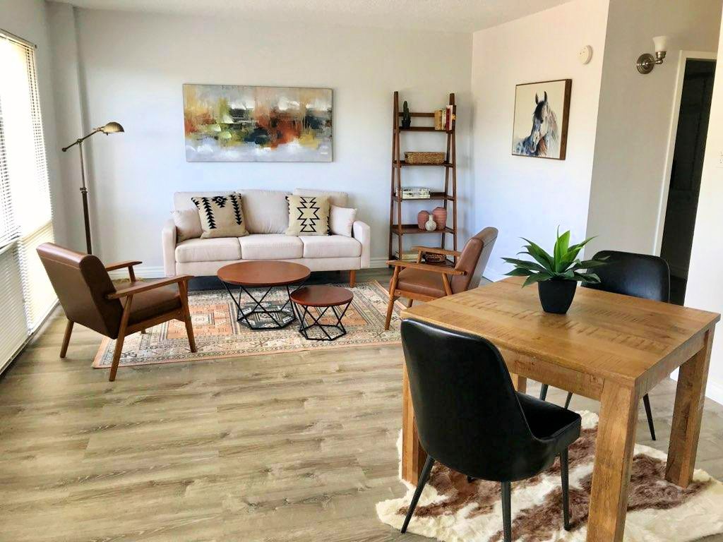 A cozy living room with modern decor, featuring a sofa, coffee table, dining area, and stylish artwork.