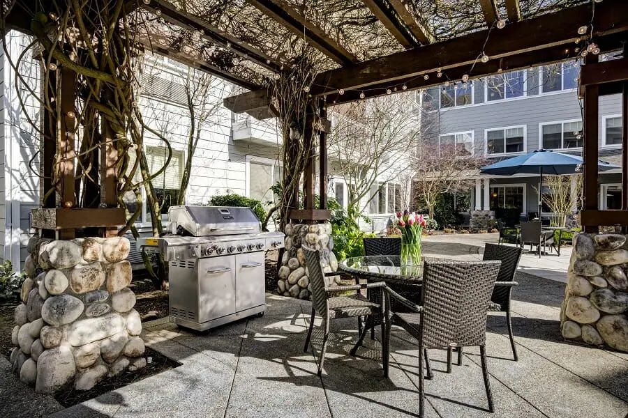 A cozy outdoor patio with a pergola, seating area, and grill in a residential setting.