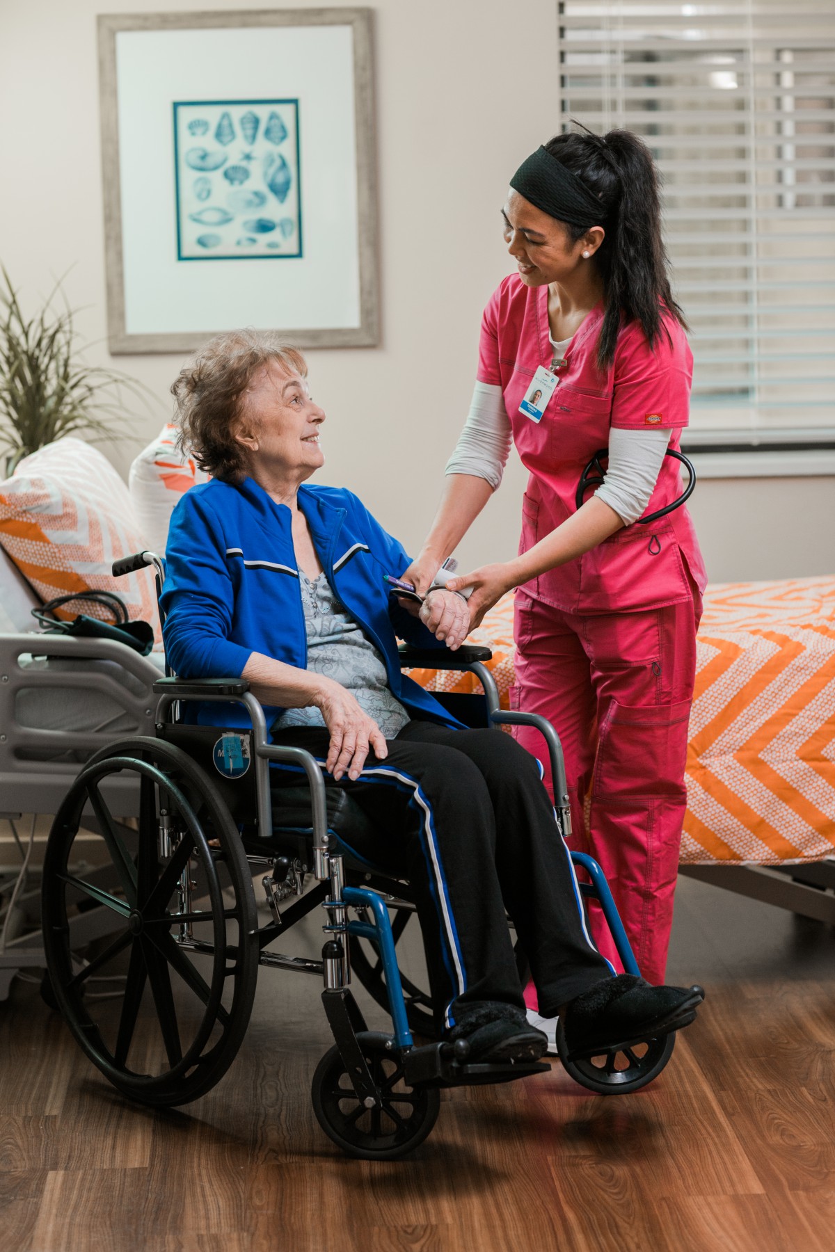 A nurse assists an elderly woman in a wheelchair in a healthcare setting.