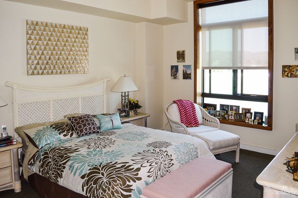 Cozy bedroom with floral bedding, a comfortable chair, and natural light from the window.