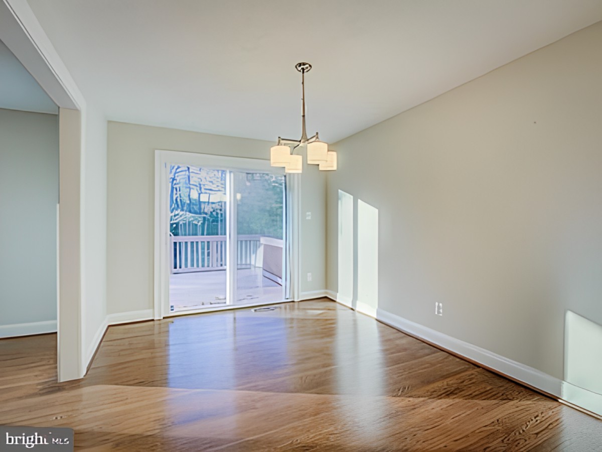 Bright and empty dining room with hardwood floors and a sliding glass door.