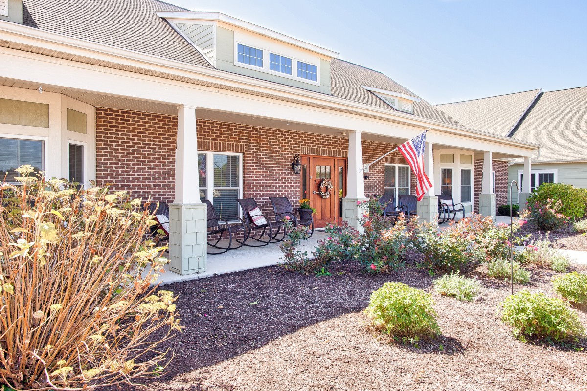 A brick house with a front porch adorned with rocking chairs and an American flag.