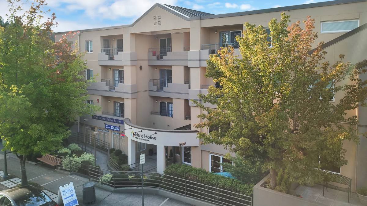 A residential apartment building with multiple balconies and a tree in the foreground.