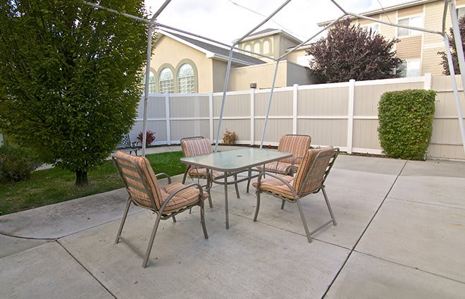A cozy outdoor patio setup with a table and four chairs surrounded by a white fence.