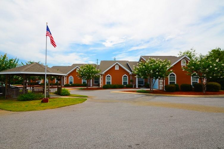 A complex of red brick buildings with an American flag flying in the front, surrounded by trees and a paved driveway.