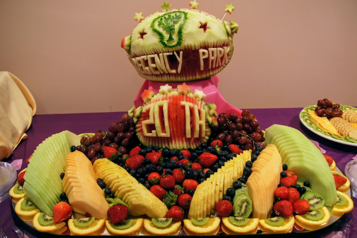 A vibrant fruit carving display celebrating a 20th anniversary with intricately carved watermelons and an assortment of fresh fruits.
