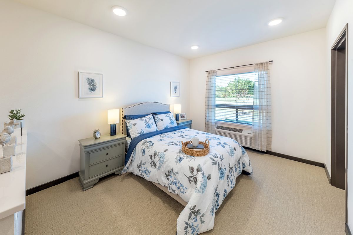 A neatly organized bedroom with floral bedding and ample natural light.