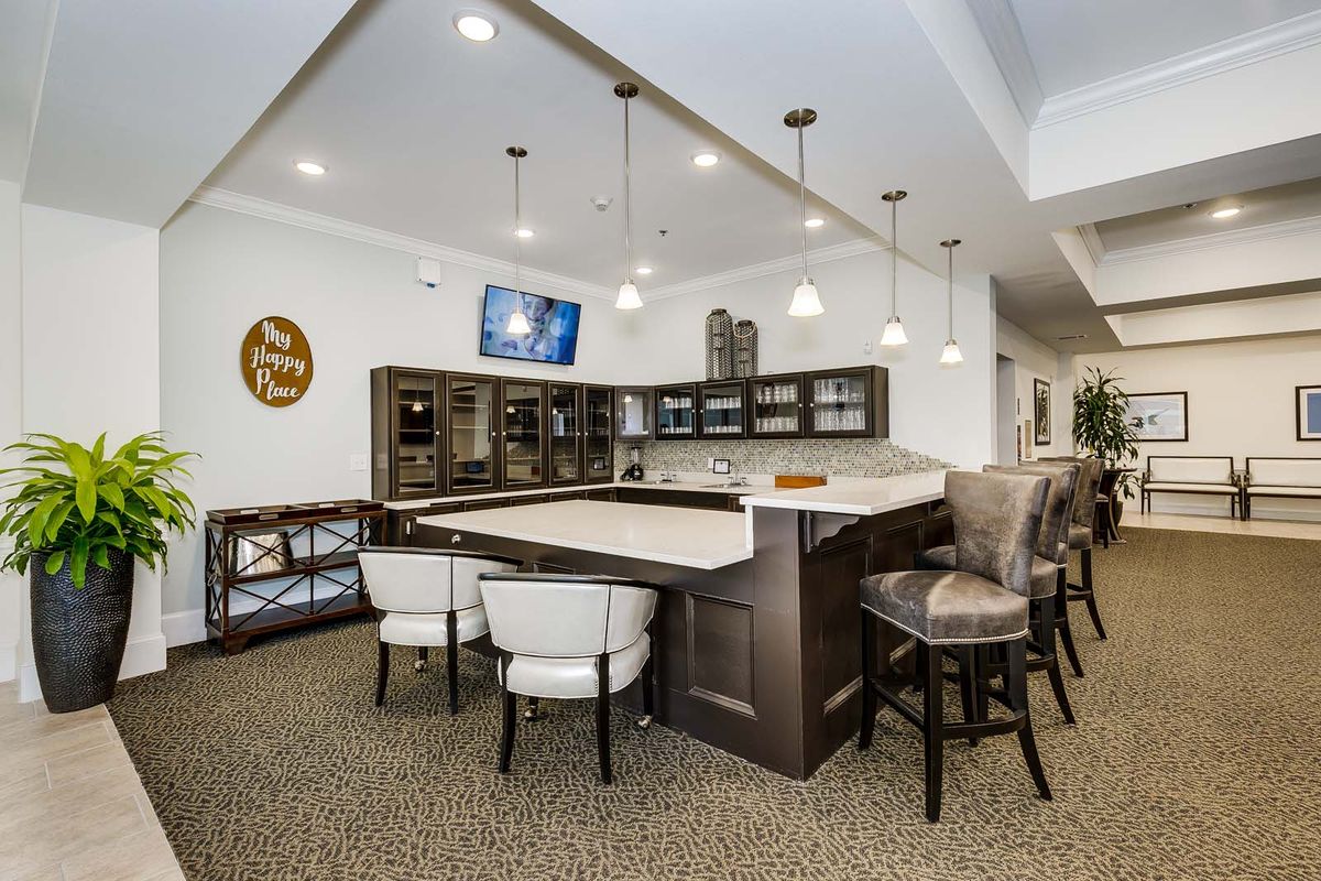 A modern kitchen interior featuring a countertop with bar stools, pendant lighting, and a wall-mounted television.