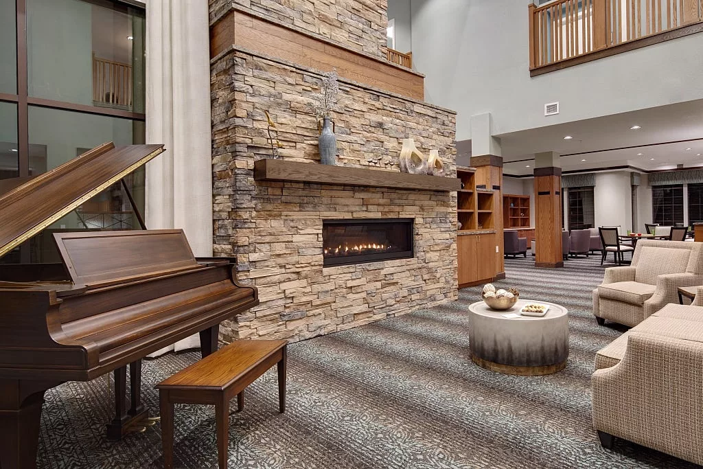 A cozy living room with a modern stone fireplace and a piano.
