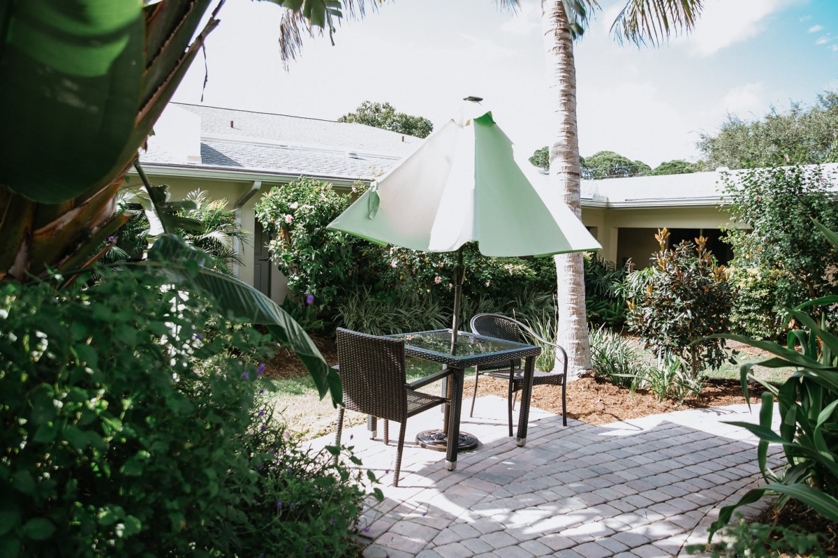 A tranquil patio setting with a table, chairs, and an umbrella surrounded by lush greenery.
