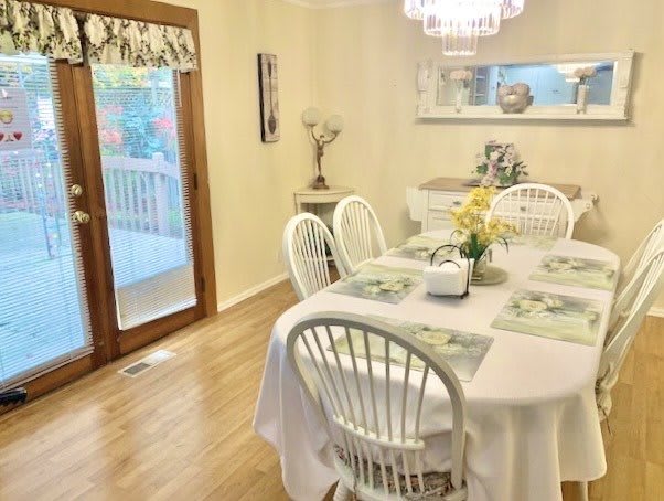 A cozy dining room with a round table, surrounded by white chairs and adorned with fresh flowers under a chandelier.