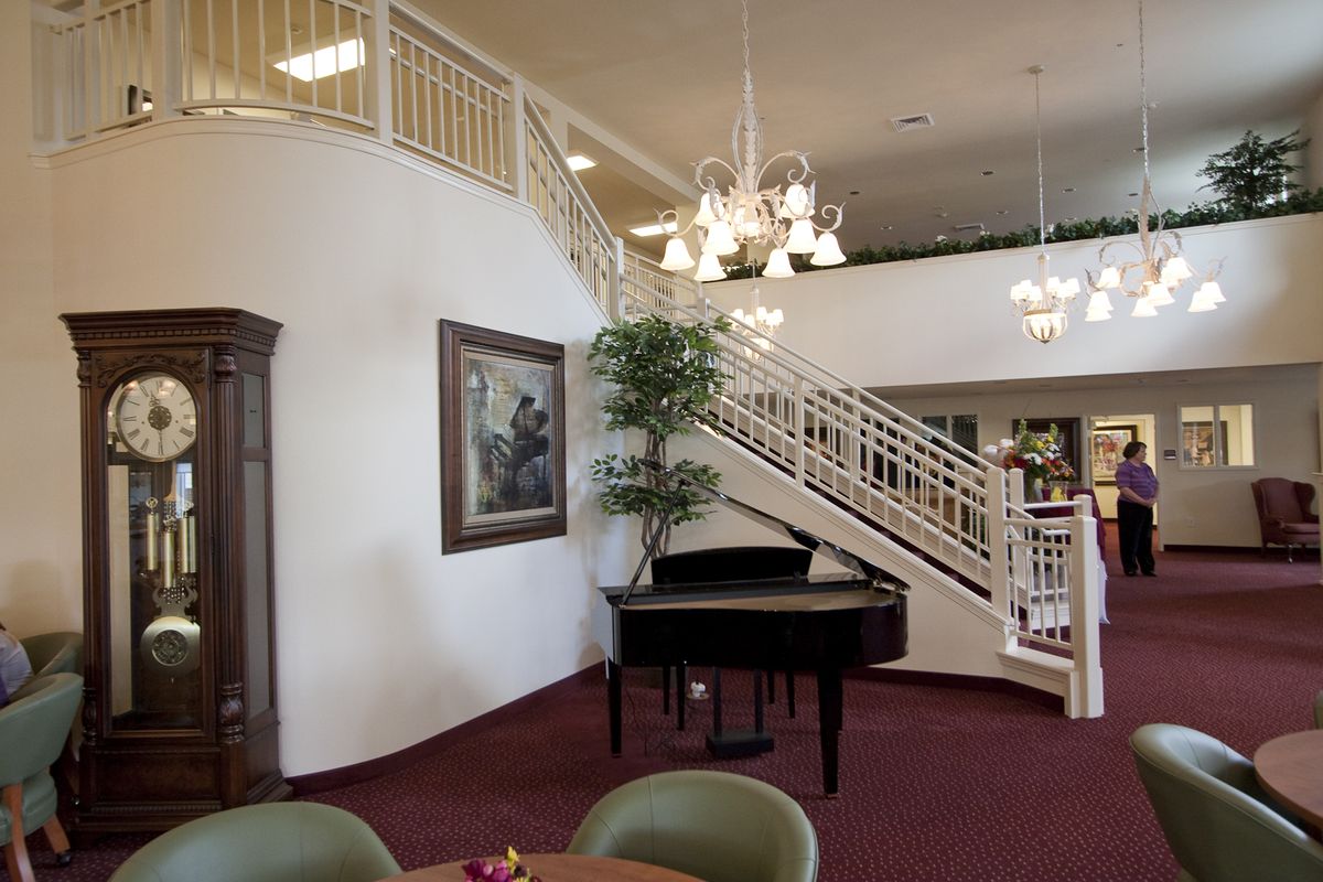 A spacious interior featuring a grand piano and elegant staircase under ornate chandeliers.