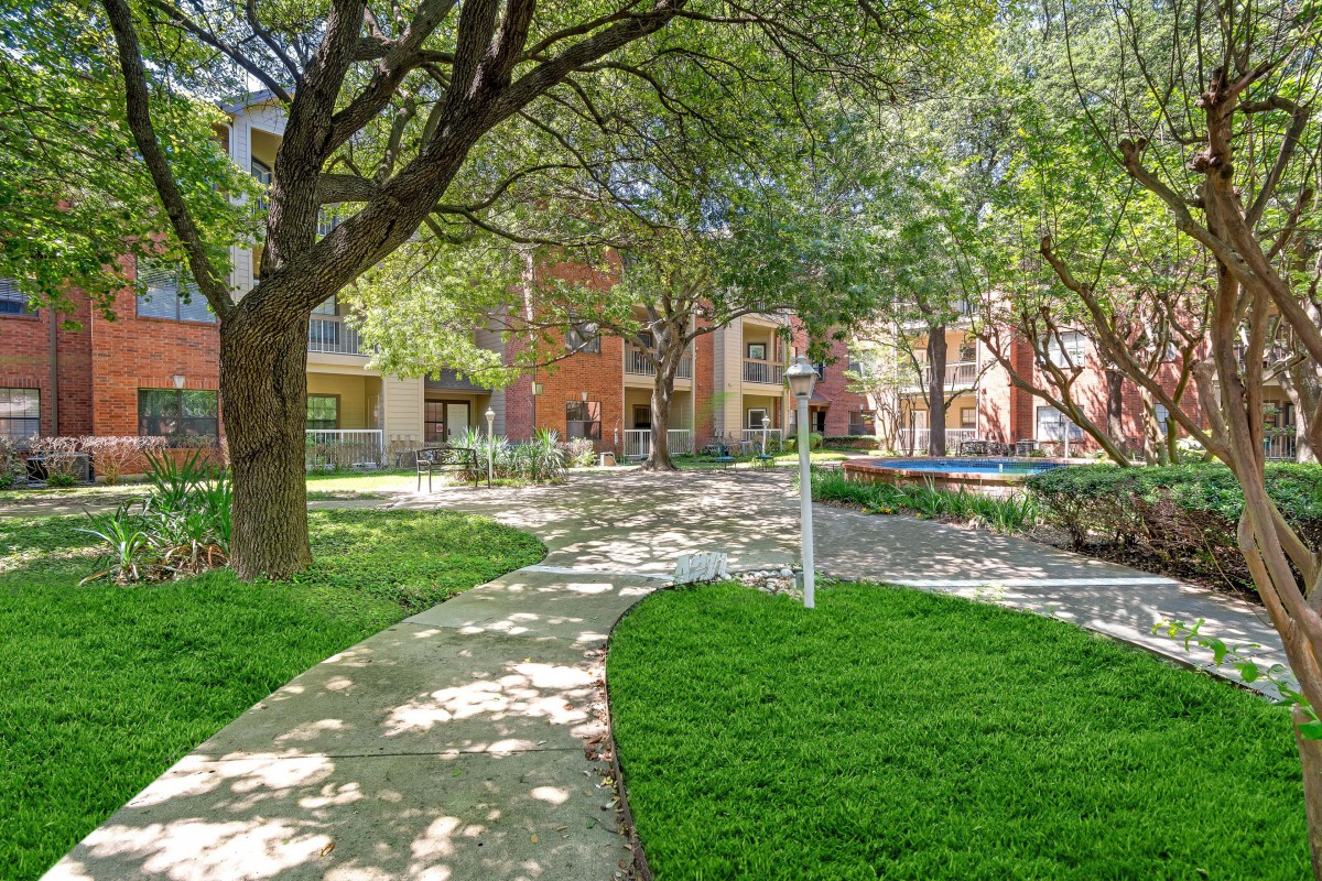 A picturesque view of a residential apartment complex with a well-maintained pathway and lush green landscaping.