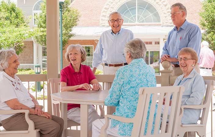 A group of seniors enjoying a conversation outdoors in a community setting.