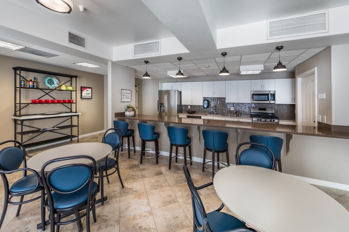 A modern kitchen and dining area with barstools and tables, featuring contemporary lighting and decor.