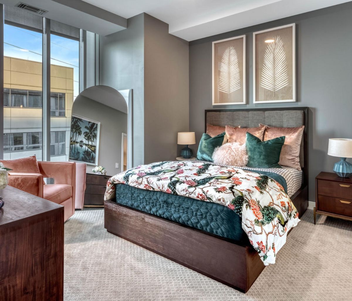 A modern bedroom with stylish decor, featuring a bed with floral bedding and large windows.