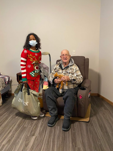 A joyful moment shared between a young girl in festive clothing and an elderly man, both smiling together during the holiday season.