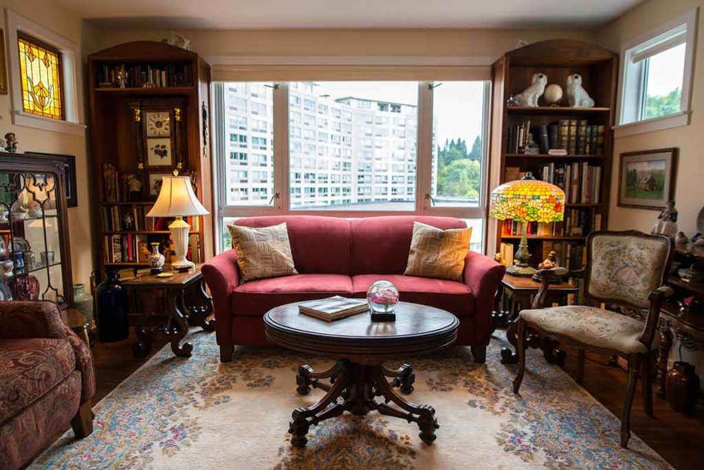 A cozy living room with a red sofa, surrounded by bookshelves and illuminated by soft natural light through the window.